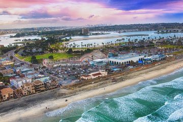 Coast of San Diego with strip of beach running along the ocean. Beach houses in grid neighborhood and roller coaster. Lakes in the distance.