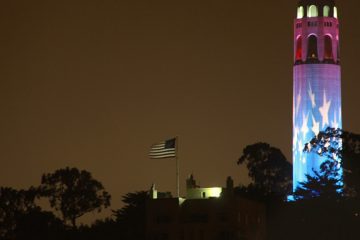 American flag blowing atop a hill with stars projected on a tower.