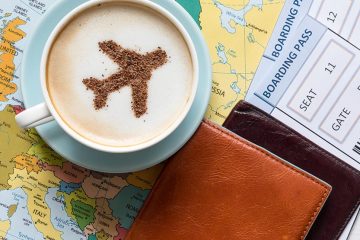 Coffee grounds in the shape of a plane on top of a latte, sitting on a map with leather wallets and boarding passes.