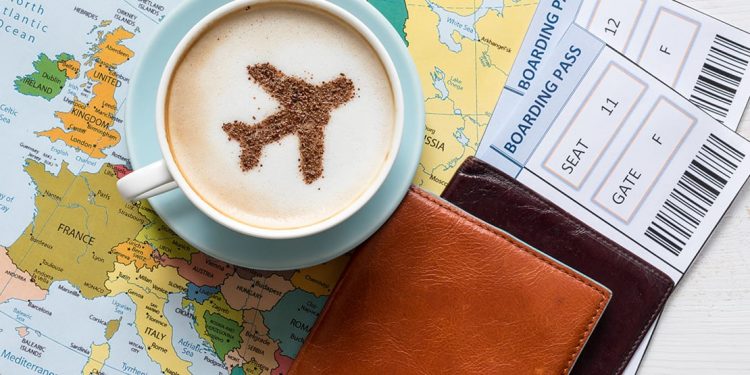 Coffee grounds in the shape of a plane on top of a latte, sitting on a map with leather wallets and boarding passes.