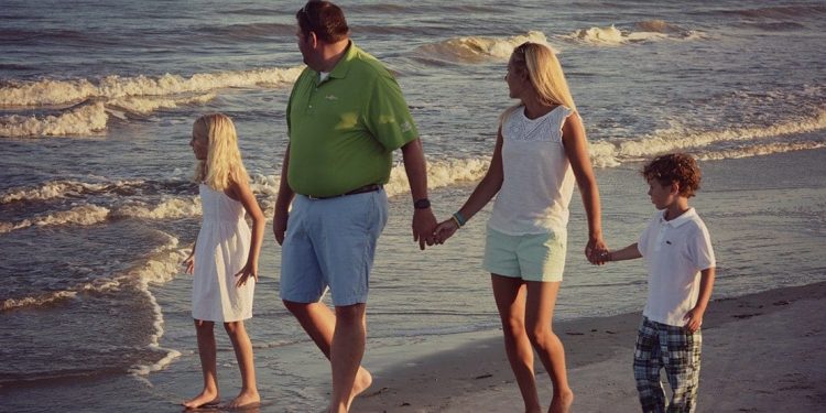 Little girl, dad, mom, and little boy holding hands and walking on the beach.