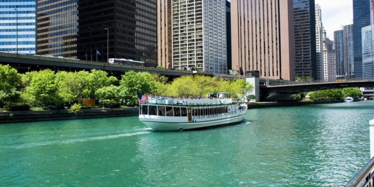 A tour boat motors down the Chicago River with sky rises in the background.