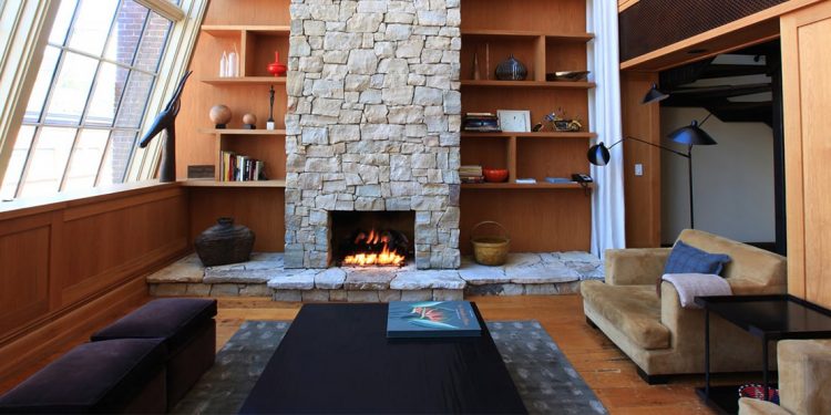 Sitting room with stone fireplace set in wooden bookshelves with large coffee table and velvety brown couch.