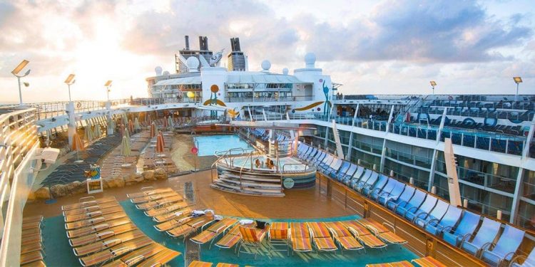 Top deck of cruise ship with wooden floor, lounge chairs, and swimming pool.