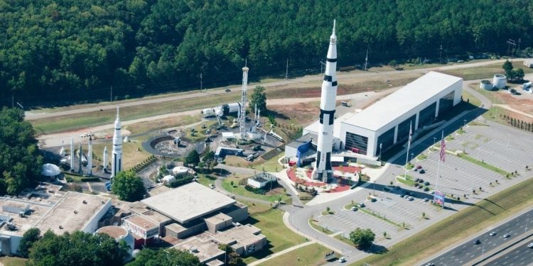 Overhead view of the US Space and Rocket Center: rectangular building, rocket, large parking lot, and various towers.