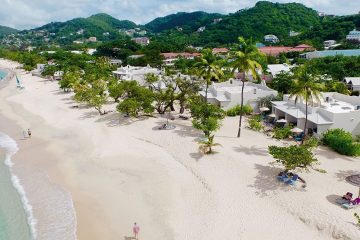 White sand beach with clear blue water, palm trees, and white buildings.