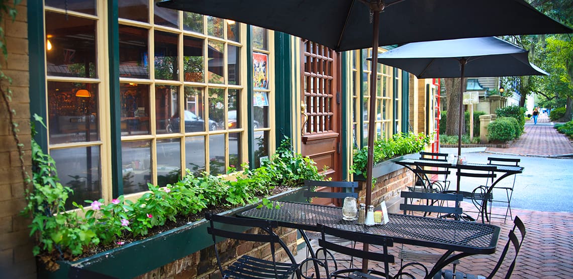 Cozy and picturesque street cafe (bistro) with window boxes, chairs, tables and umbrellas. Brick sidewalk, French windows and front door. City life; cafe society; small restaurant; Savannah, Georgia.