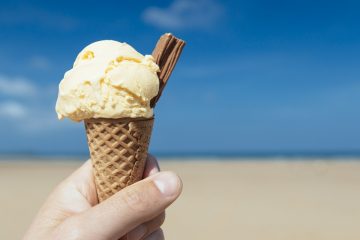 Vanilla ice cream cone held up against the beach and ocean.