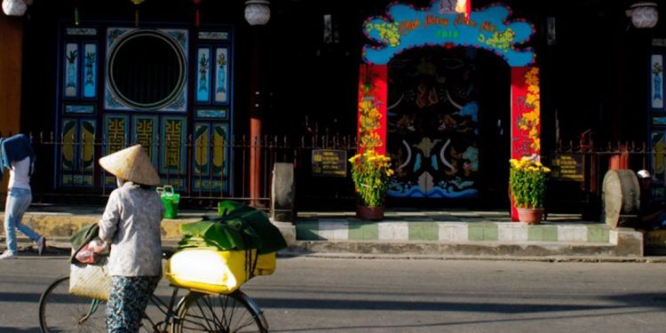 Woman walking beside her bike outside of a colorful building in Hoi An.