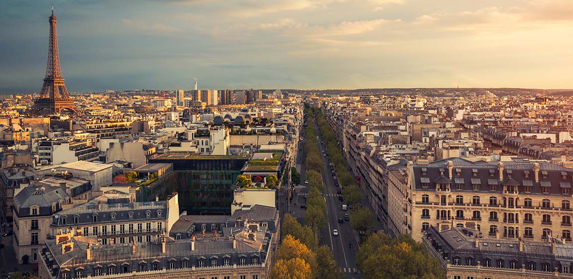 A view of Paris from above, looking down a street lined with trees with the Eiffel tower in the background.