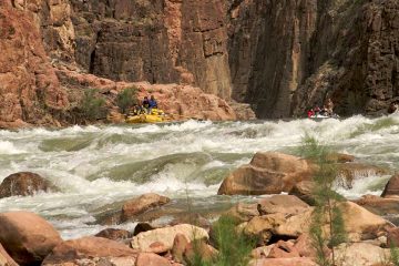 Three rafts approach a set of rapids with rock wall behind them.