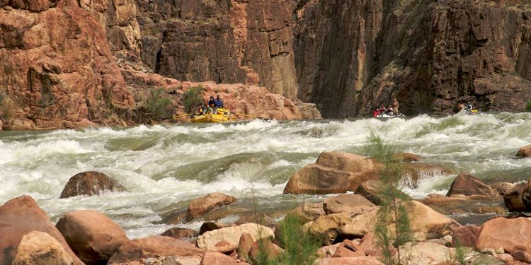 Three rafts approach a set of rapids with rock wall behind them.