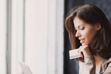 A woman holds a credit card as she looks intently at the screen of her laptop.