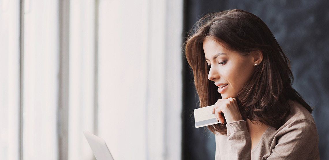 A woman holds a credit card as she looks intently at the screen of her laptop.