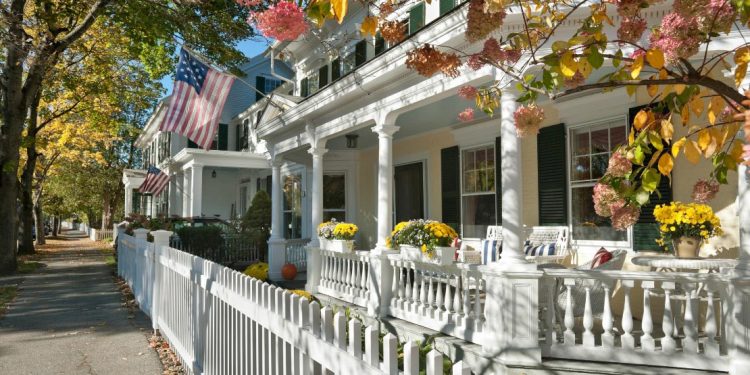 Quintessential American houses with picket fences with American flags hanging off.