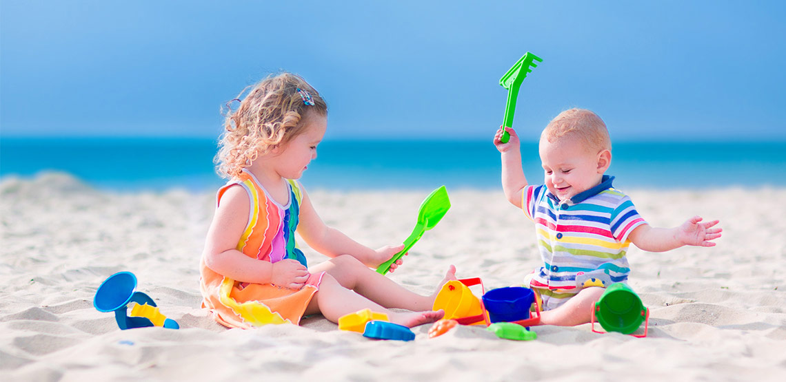 Two young children sitting and playing on the beach.