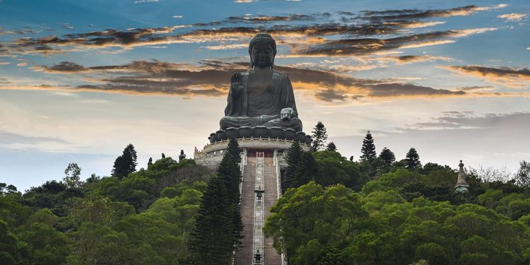 Big Buddha is a massive statue of Buddha sitting atop a mountain covered in trees with a staircase leading up to its base.
