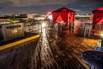 An outdoor dance floor on the top of a building at night with red VIP tents and a DJ station.