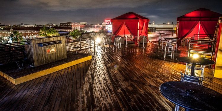 An outdoor dance floor on the top of a building at night with red VIP tents and a DJ station.