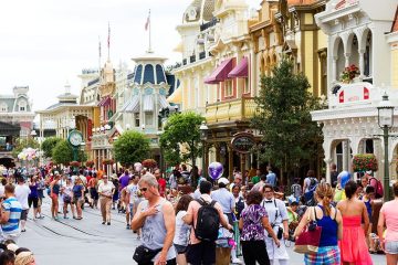 A crowded street at Disney World lined with streetlamps and colorful storefronts.