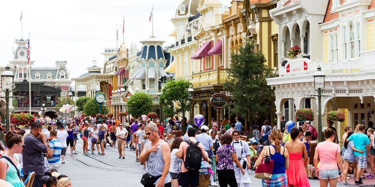 A crowded street at Disney World lined with streetlamps and colorful storefronts.