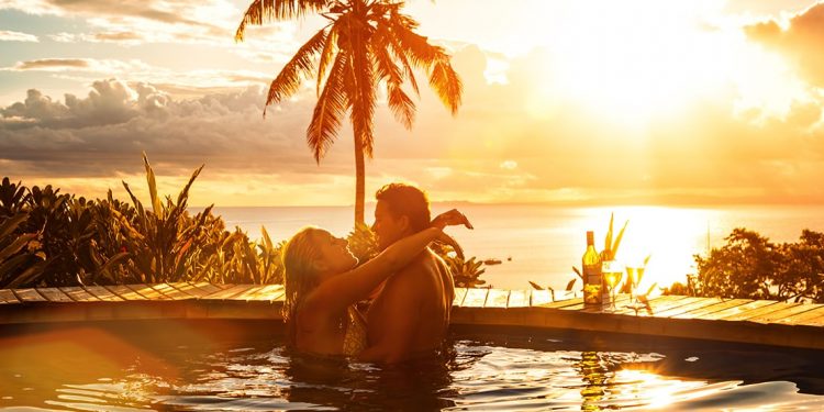 A couple embraces in a hot tub with a view of palm trees and the ocean.