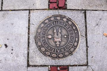 Metal marker that reads 'Boston Freedom Trail' set in a paving stone.