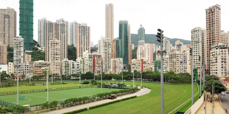 A grass track for horse racing with a soccer field in the middle and towering skyscrapers all around.