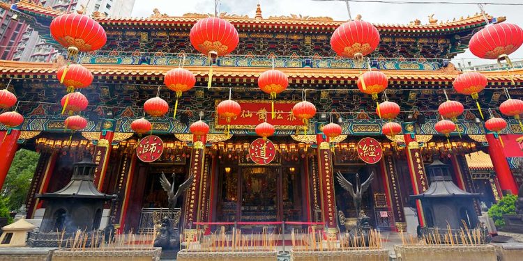 The outside of a temple with green and red decor and red lanterns hanging from overhead wires.