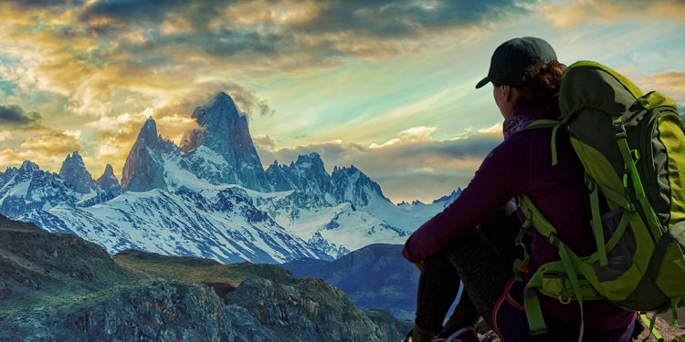 Woman with backpack admiring far off, snow capped mountains.