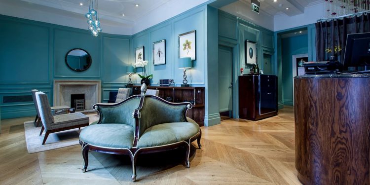 The front desk and a teal-decorated lounge area inside The Levin Hotel in London.