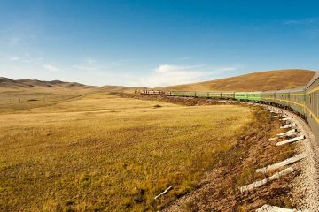 Train winding along a hilly landscape covered in yellowed grass.
