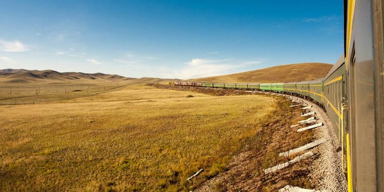 Train winding along a hilly landscape covered in yellowed grass.