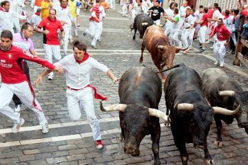 Men wearing red and white running alongside bulls down the street.