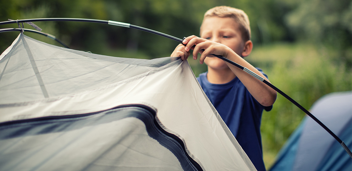 Young boy clips a clip to a tent pole.
