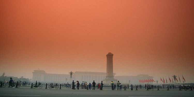 Foggy morning with orange sky. Tower monument in front of stately building. People milling about out front.