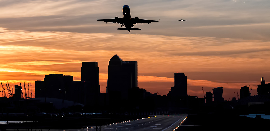 Plane taking off of runway with buildings silhouetted in background.