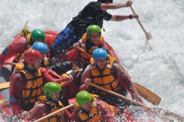 Seven rafters and a guide in a red raft with white water all around.