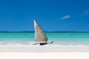 A traditional dhow boat sits in the turquoise water off Zanzibar.