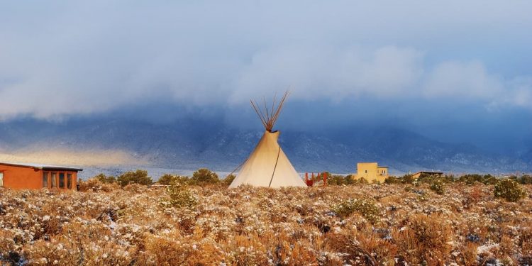Teepee erected in a field surrounded by sage bushes and snow in Taos, New Mexico