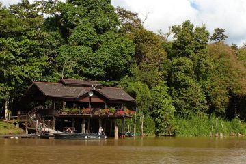 Lodge at the side of a river with boat out front.