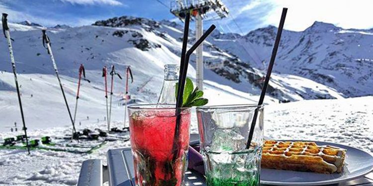 Drinks and waffle with skis and mountains in background.