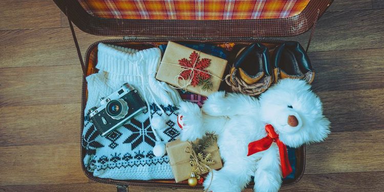 Two wrapped gifts in suitcase with camera, sweater, boots and teddy bear.