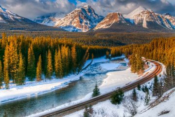 Snow capped mountains and trees, railway track along river.