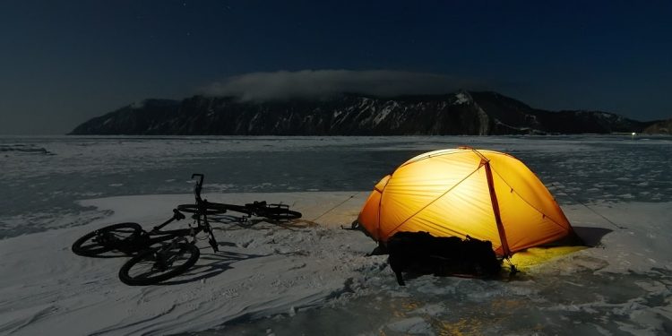 An orange tent and bikes lies on the surface of frozen lake at night.