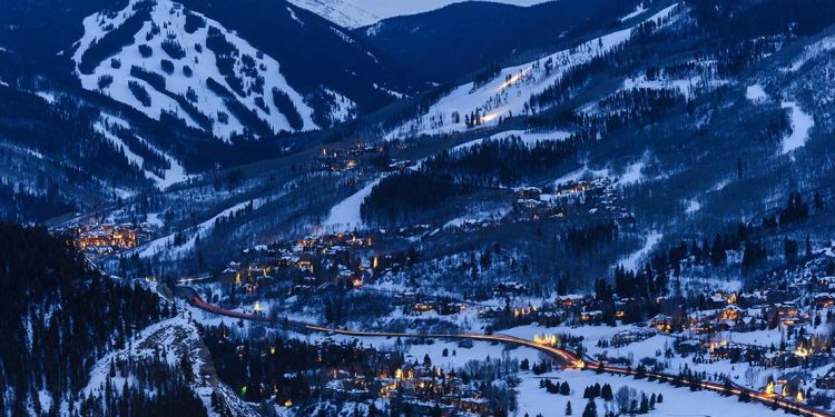 Valley with brightly lit cabins and ski slopes on surrounding mountains.