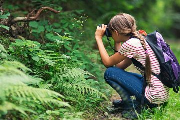 Young girl crouching to take photo of a plant