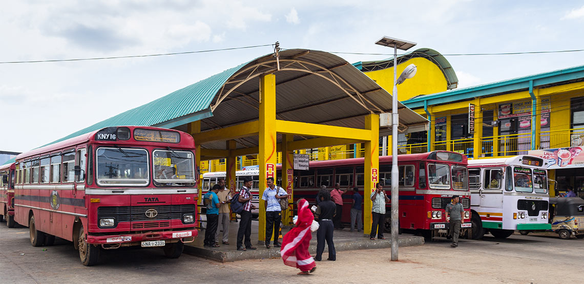Bus station in India with red buses and people loitering.