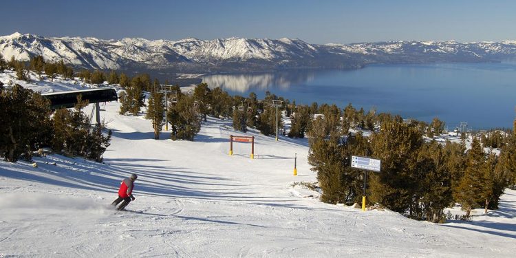 Skier on a run with lake and mountain range in background.