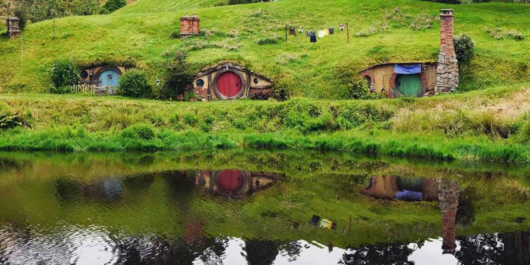 Three hobbit holes set in hillside with pond in front